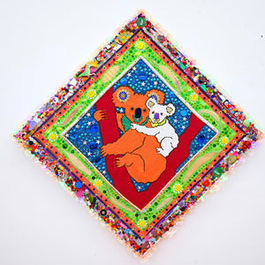 Paul Yore, Koalas (Orange & White), 2025, acrylic yarn needlepoint embroidery on canvas, felt, fabric, ribbon, cotton thread, laminated leaves, plastic teddy bear eyes, tassels, trim, buttons, beads, sequins, glitter, glass, shells, found objects, eyelets, LED light, wood, adhesive, fixtures, and enamel, 92 x 92 x 5 cm
