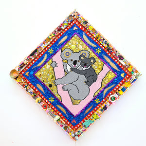 Paul Yore, Koalas (Light Grey & Gunmetal), 2025, acrylic yarn needlepoint embroidery on canvas, felt, fabric, ribbon, cotton thread, laminated leaves, plastic teddy bear eyes, tassels, trim, buttons, beads, sequins, glitter, glass, shells, found objects, eyelets, LED light, wood, adhesive, fixtures, and enamel, 91 x 91 x 5 cm
